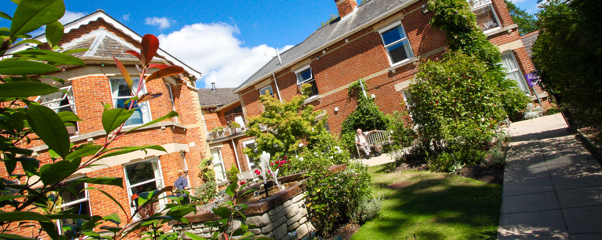 View of the gardens with green bushes and plants blooming with the care home in the background