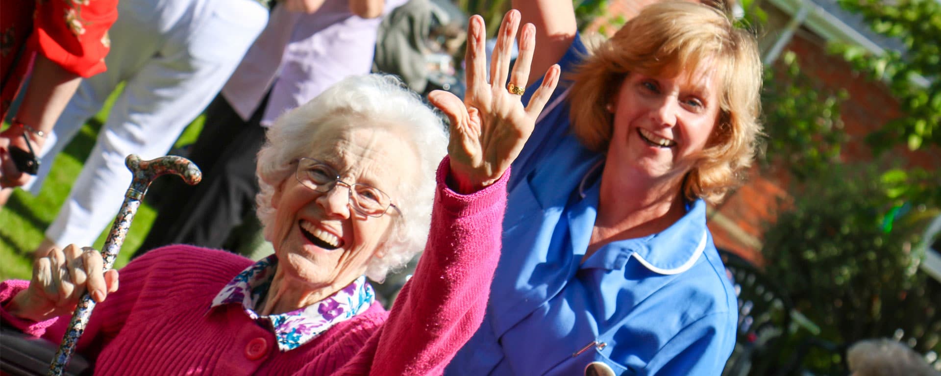 Resident and nurse waving and smiling in the garden